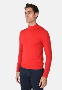Maglione a collo alto rosso in maglia con scollo e polsini a coste, design aderente e tessuto liscio, abbinato a pantaloni blu scuro.