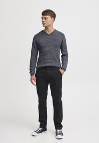 Grå strikket genser med lange ermer og v-hals, svarte slim-fit bukser og svarte sneakers med hvite såler. Glatt tekstur, tettsittende design.