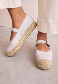 Hellbeige Espadrilles mit einem Obermaterial aus Canvas und einer geflochtenen Jutesohle. Verfügt über einen Riemen über dem Spann und eine dekorative Schnallenakzentuierung.