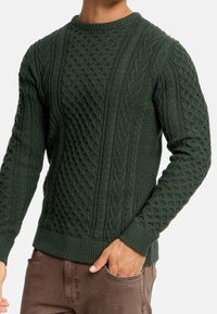 Donkergroen gebreid sweater met verschillende textuurpatronen, waaronder kabels en bulten, met ribgebreide manchetten en zoom.