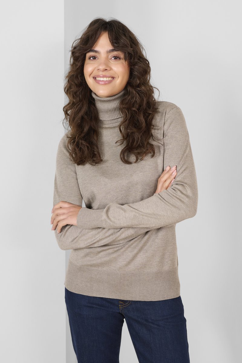 Beiger Rollkragenpullover mit gerippten Bündchen und Saum, aus weichem Material gefertigt. Das Modell trägt ihn mit dunkelblauen Jeans und steht vor einem hellen Hintergrund.