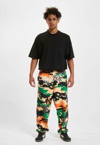 Sort oversized t-shirt parret med multifarvede camouflage sweatpants med orange, grønne og sorte mønstre. Sorte sneakers fuldender looket.