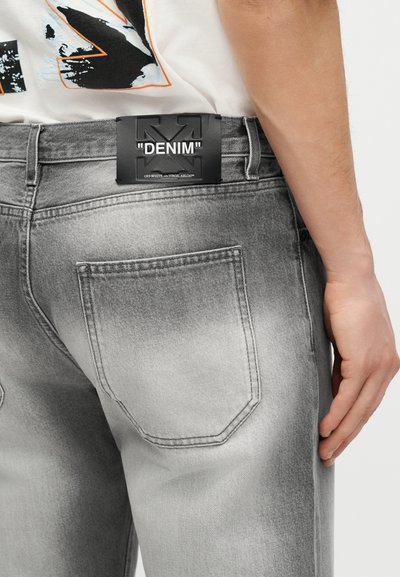 Άτομο που φοράει ξεθωριασμένο γκρι τζιν με μια μαύρη ετικέτα που γράφει "DENIM" στη πίσω μέση.