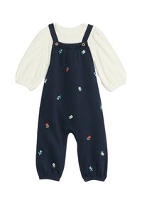 Marinblå bomullsbyxa med broderade blommor i rosa, rött och grönt. Har justerbara axelremmar, träknappar och en krämfärgad långärmad tröja under.