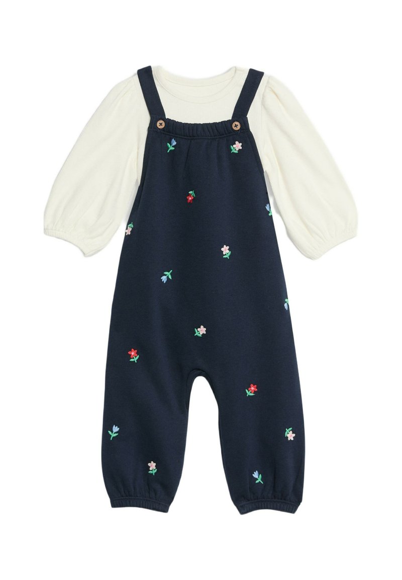 Marinblå bomullsbyxa med broderade blommor i rosa, rött och grönt. Har justerbara axelremmar, träknappar och en krämfärgad långärmad tröja under.