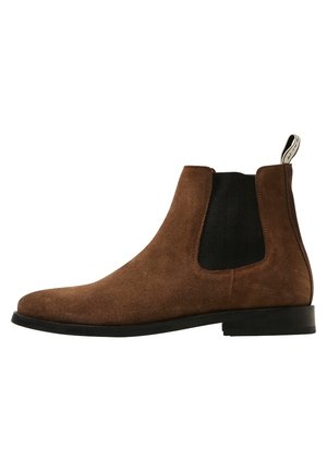 Bota Chelsea de ante marrón con panel lateral elástico negro, suela negra, tacón bajo y tira para tirar en la parte trasera.