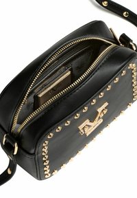 Černá kožená kabelka přes rameno se zlatými cvočky a kováním. Má zipový otvor odhalující kapsy na karty a podšívku uvnitř.