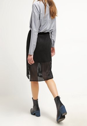 Jupe midi plissée à rayures noires en tissu léger, associée à une chemise grise et des bottines à talon bloc bleu.