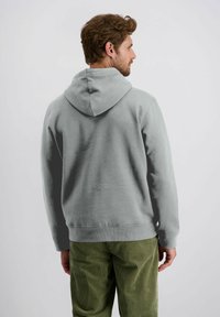 Grijze hoodie met een trekkoordkap, ontspannen pasvorm en zachte structuur. De mouwen en zoom zijn geribbeld. Draagt men in combinatie met groene corduroy broeken.