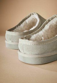 Chaussons en textile gris avec doublure intérieure en peluche, extérieur doux, forme ronde et coutures renforcées sur les bords et la semelle.