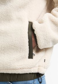 Crème-kleurige fleece jacket met een zachte textuur, voorzien van groene accenten, elastische manchetten en een voorvak met een ritssluiting detail.