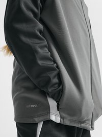 Person trägt eine grau-schwarze Jacke mit Reißverschlusstaschen, Hand in der Tasche und dem Schriftzug „BEE COOL“ an der unteren Seite.