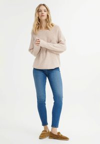 Light pink, textured sweater with long sleeves, paired with fitted blue jeans and brown suede loafers featuring gold hardware accents.