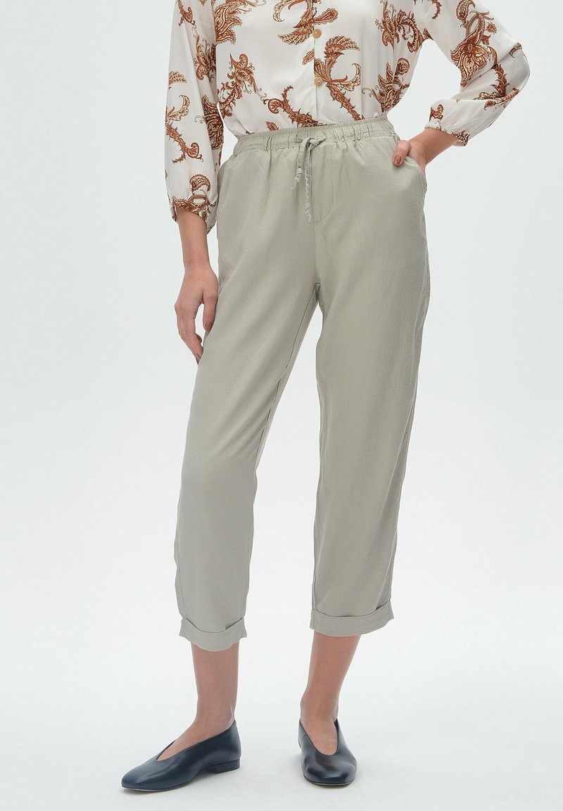 Jasnoszare, zwężane spodnie z elastycznym pasem i sznurkiem, z podwiniętymi mankietami i gładką fakturą. W połączeniu z ciemnymi balerinami.