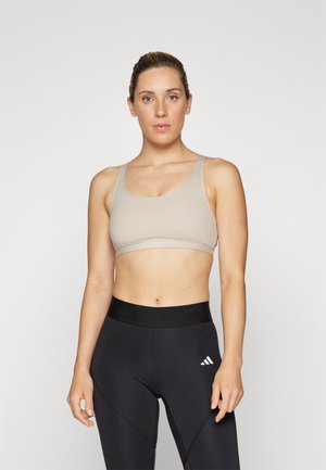 Soutien-gorge de sport beige avec des bretelles larges, texture lisse et design minimal, associé à un legging noir taille haute avec un logo.