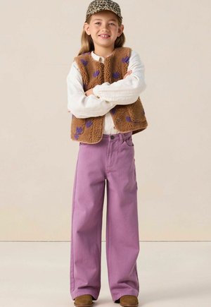 Gilet en polaire marron avec des motifs de cœurs violets, chemise à manches longues blanche, pantalon large lavande et casquette à imprimé léopard.