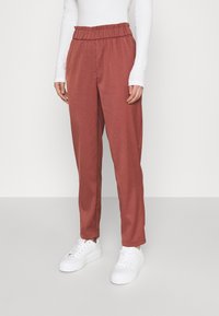 Roestkleurige, lichtgewicht, loszittende broeken met een elastische tailleband, gecombineerd met witte sneakers en een langemouwen top.