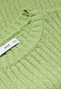 Vihreä neulepusero, jossa on ribbitetty kaula-aukko ja teksturoitu kuvio, sekä kangasmerkki, josta löytyy brändi- ja hoito-ohjeet.