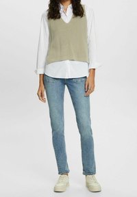 Ljusgrön ribbad stickad väst över en vit skjorta med knappar, tillsammans med åtsittande ljusblå jeans och beige sneakers. Enkel och avslappnad stil.