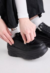 Baskets à plateforme noires avec une tige en cuir lisse, une fermeture éclair et une semelle en caoutchouc texturée. Dotées de ferrures argentées et d'un design en couches.
