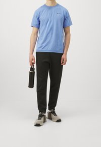 Camiseta Nike azul claro, pantalones jogger negros, zapatillas grises y negras, y una botella de agua negra. Ropa deportiva casual con un diseño sencillo.