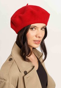 Beret roșu din lână, cu o formă moale și rotunjită și cu un tab superior. Purtați-l cu un trench coat bej deschis, având nasturi mari și guler.