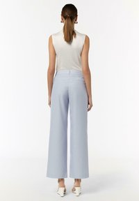 Helleblaue weit geschnittene Hose mit glatter Textur, hoher Taille und Gesäßtaschen, kombiniert mit einem ärmellosen weißen Oberteil und weißen Schuhen.