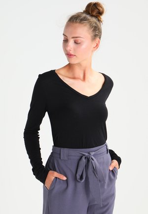 Haut noir à manches longues avec un design en V, associé à un pantalon gris taille haute avec une ceinture à nouer et des poches latérales.