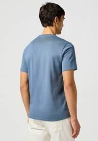 Camiseta de algodón azul de manga corta con cuello redondo. Textura suave y diseño simple, vista desde la parte posterior. Estilo minimalista.