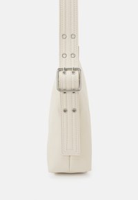 Sac en cuir beige fin vu de côté avec une sangle ajustable munie d'une boucle métallique et d'œillets.