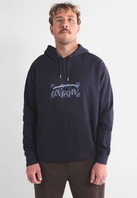 Sweat à capuche bleu marine en mélange de coton, avec une poche kangourou à l'avant et un logo Oxbow graphique en bleu clair.