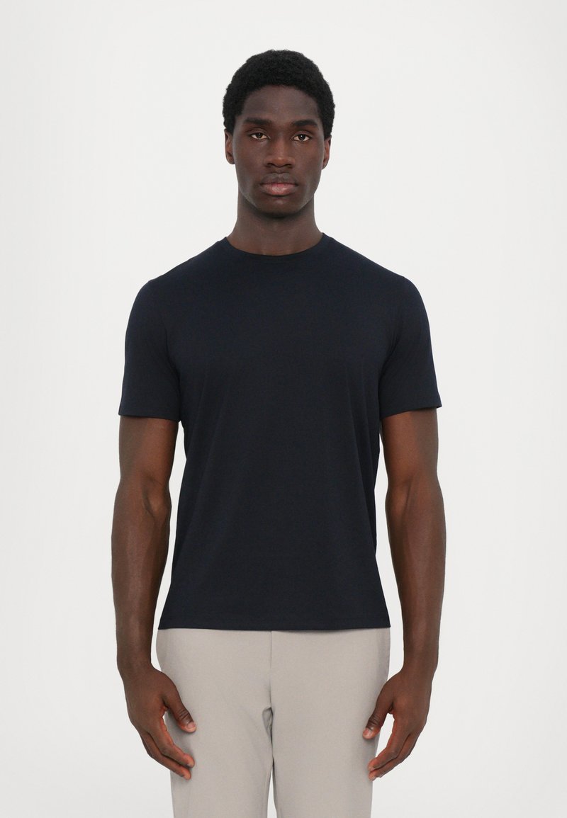 Marineblaues T-Shirt mit kurzen Ärmeln aus glattem Stoff, rundem Halsausschnitt, figurbetontem Schnitt und minimalen Nähten. Das Modell steht vor einem neutralen Hintergrund.