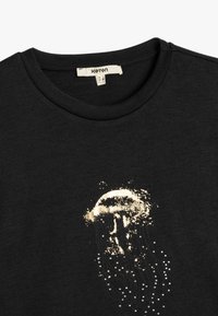 Schwarzes Baumwoll-T-Shirt mit Rundhalsausschnitt, mit einem goldenen Qualle-Graphic-Design und weißen punktierten Akzenten, glatte Textur, lässige Passform.