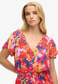 Abito floreale con sfondo rosso decorato da fiori rosa, gialli e blu, scollatura a V, maniche corte e vita elasticizzata.