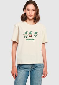 Cremefarvet bomulds t-shirt med et grafisk motiv af tre nissekarakterer med grønne hatte, grønternede og rødrutede detaljer samt teksten "Jule Trio."