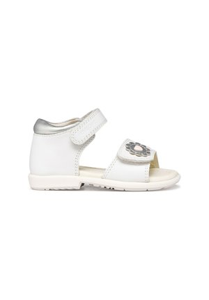 Sandalia blanca para niño pequeño con tacón plateado, dos correas ajustables y decoración de flor en la correa delantera, vista lateral sobre fondo blanco.