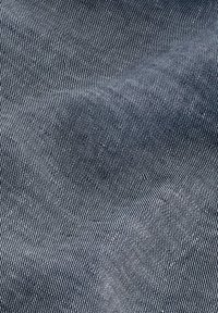 Tissu en denim bleu foncé avec une texture subtile en chevrons. Présente de fines lignes verticales créant une surface lisse et légèrement brillante.