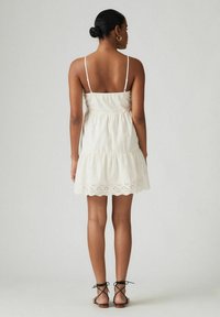 Vit bomulls sundress med justerbara spaghetti axelremmar, lagerdesign och broderi i ögonfransar vid fållen. Matchad med svarta remsandaler.