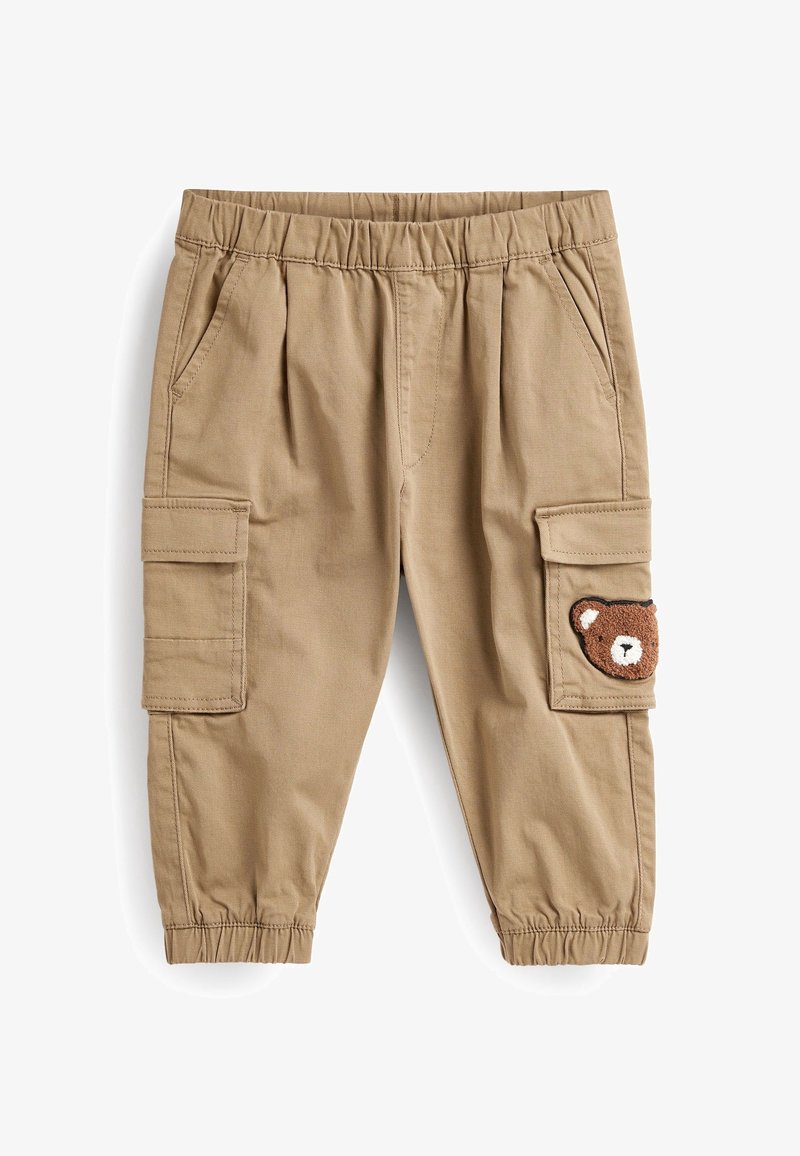 Pantalon cargo en coton couleur beige avec taille élastique, doté de poches latérales et d'un écusson en forme d'ours brun texturé sur la jambe droite.