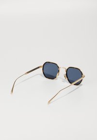 Ochelari de soare octagonali cu lentile închise la culoare, cadru din metal auriu și accente din sidef pe margini. Temele subțiri, curbe, cu detalii texturate.