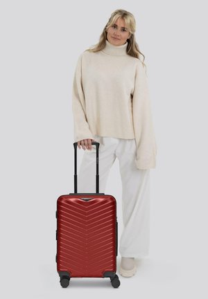 Valise rigide rouge avec un motif en chevrons, deux roues noires, poignée extensible et poignée latérale pour une prise en main facile. Design minimaliste.