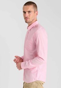 Camicia a maniche lunghe di un rosa chiaro con strisce verticali, colletto a punta, taschino singolo sul petto e vestibilità standard. Texture del tessuto liscia.