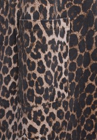 Leeuwenhuidprint stof, met verschillende tinten bruin en zwarte vlekken. Inclusief een klein borstzakje met een strakke stiknaad. Gladde textuur.