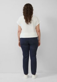 Witte kortek mouwen top met een gestructureerde afwerking, gecombineerd met navy slim-fit broek. Het model draagt witte sneakers, gezien van achteraf.