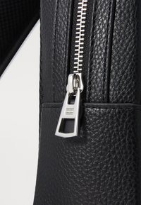 Black textured leather bag featuring a silver zipper and pull tab, highlighting the zipper's detail and craftsmanship.