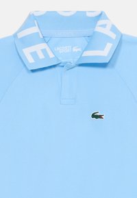 Polo bleu clair en tissu texturé, avec un col à rayures blanches, une patte de boutonnage à trois boutons et un logo crocodile vert sur la poitrine.
