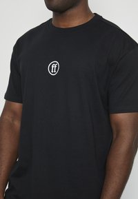 Svart bomulls t-skjorte med en hvit sirkulær logo med "ff" i midten. Stoffet ser glatt ut, med korte ermer og en klassisk passform.