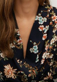 Vêtement à motif floral avec un décolleté en V profond, fond bleu marine, tissu doux, orné de fleurs bleues, blanches et rouilles.