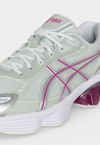 Λευκό και γκρι παπούτσι τρεξίματος ASICS με ροζ λωρίδες λογότυπου, επάνω μέρος από διχτυωτό υλικό, κορδόνια και επενδεδυμένη λευκή σόλα με μοβ υποστήριξη πτέρνας.