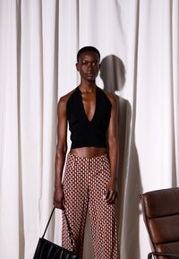 Top halter preto combinado com calças largas castanhas estampadas. Modelo segura uma bolsa preta. A textura e o ajuste realçam o design moderno.